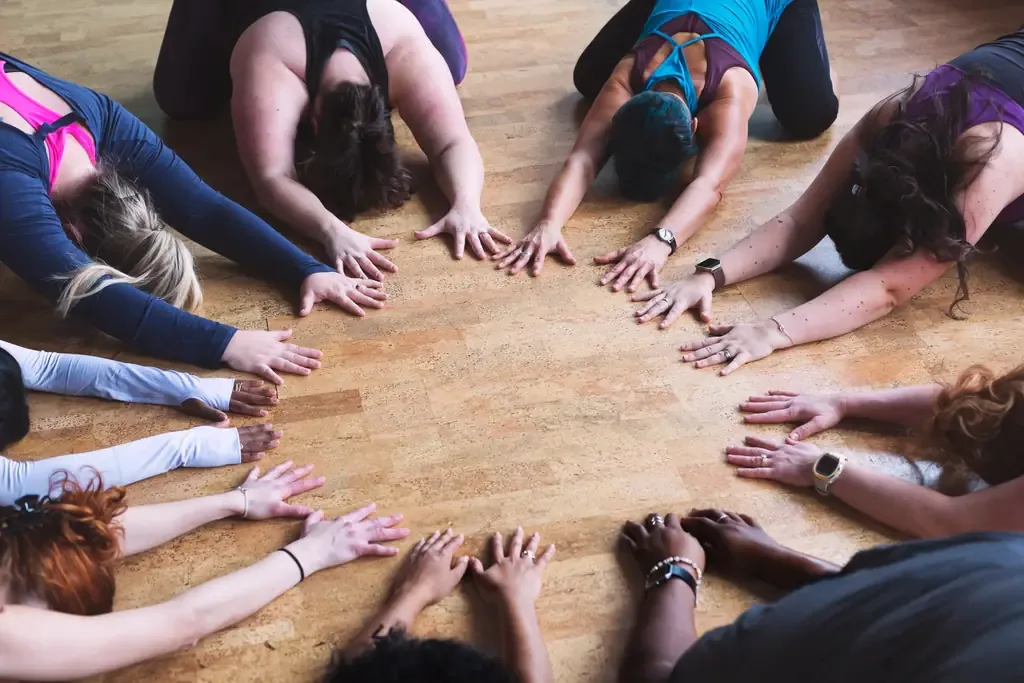 A group stretching together in a circle on the studio floor, hands reaching towards the centre